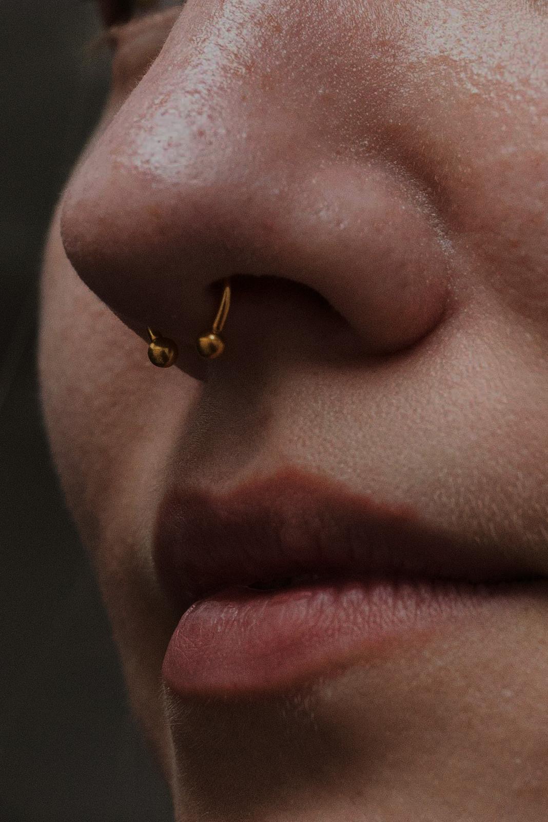 Piercing al setto con gioiello dorato realizzato da Xhenis Gega